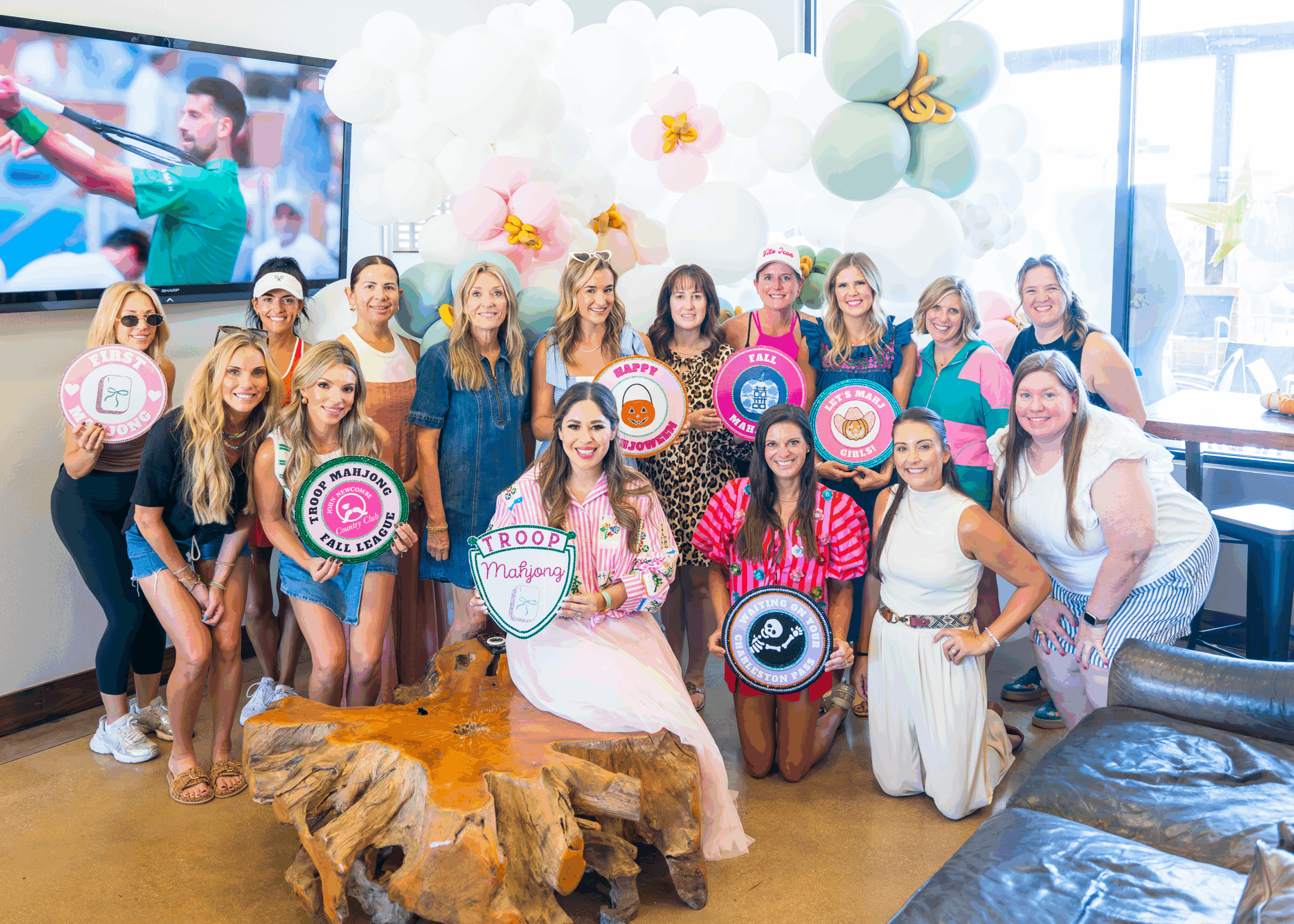 Group photo of stylishly dressed women holding Troop Mahjong merit badges and the Troop Mahjong crest logo.