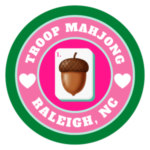 A mahjong tile with an acorn in the center of a pink circle with white text reading Troop Mahjong Raleigh, NC.